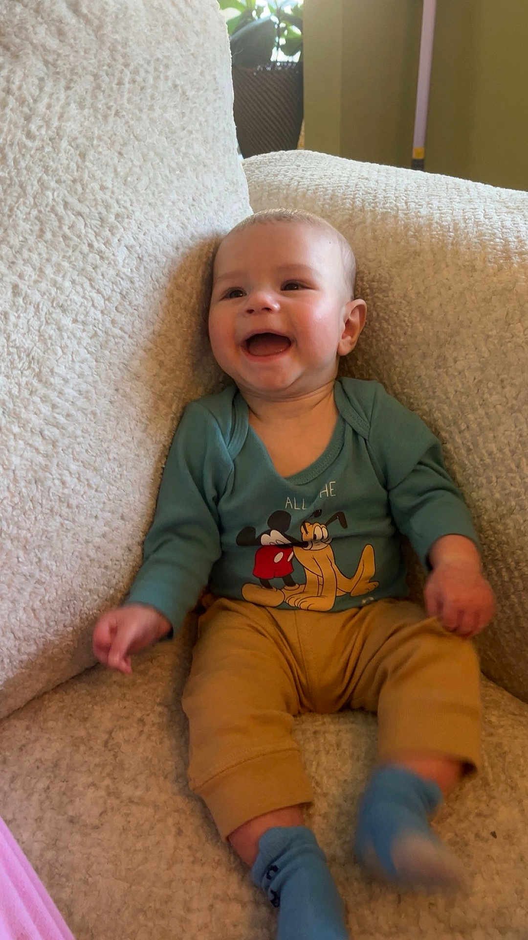 Atlas is registered to the contest to win money with this photo: baby, child, smiling, sitting, armchair, clothing, blue_socks, beige, indoor, happy, person, cute, plush, mickey_mouse, pluto, infant, cozy, portrait, young_child, furniture