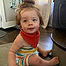 toddler, child, curly_hair, indoor, carpet, colorful_clothing, bib, smile, face, person, home, curtain, bag, floor, sitting, foot, hand, hair_bun, striped_outfit, young_child