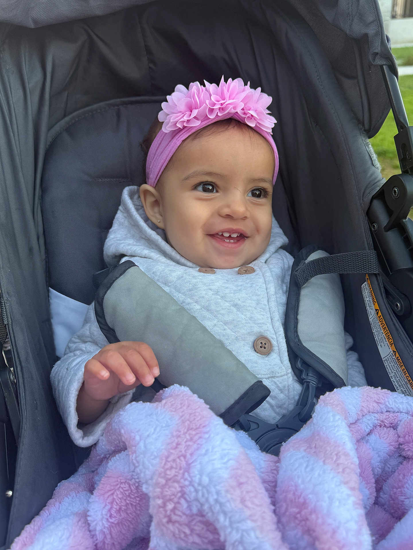 Araceli joined the competition — help win amazing prizes! baby, child, stroller, blanket, pink_headband, flower_headband, smiling, happy, cozy, cute, outdoor, clothing, jacket, seatbelt, portrait, infant, hand, face, person, warm