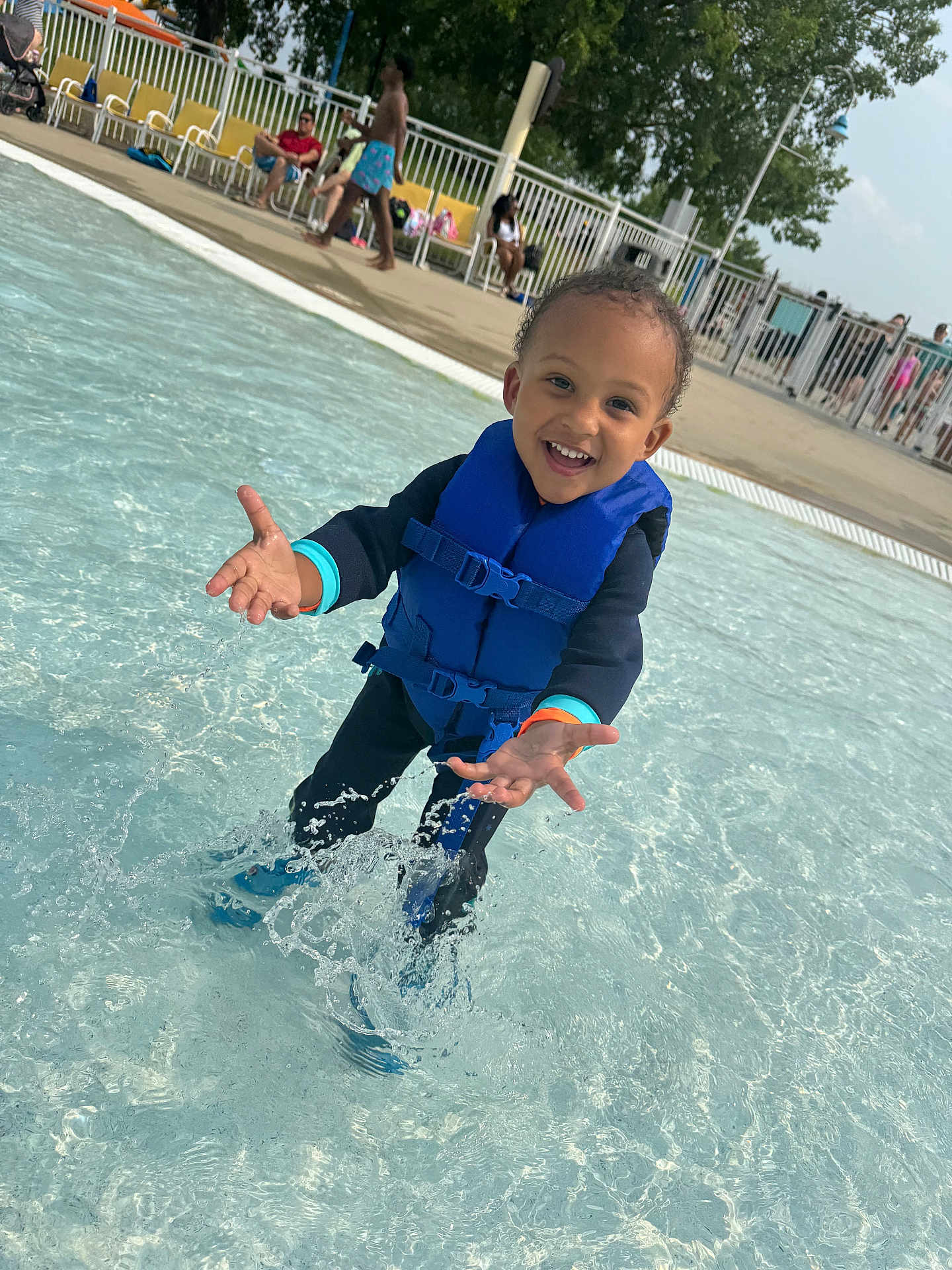 Izlan is registered to the contest to win money with this photo: child, daytime, fence, happy, leisure, life_jacket, outdoor, people, play, pool, recreation, smiling, splashing, summer, sunny, swimwear, toddler, trees, water, water_splash