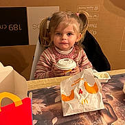 Aria a rejoint le concours — aidez-le/la à gagner de superbes lots ! child, girl, pigtails, blonde_hair, sweater, table, cup, fast_food, mcdonalds, food_packaging, happy, indoor, dining, meal, person, portrait, smile, cute, snack, cozy
