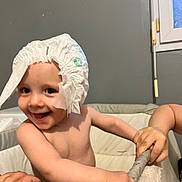 Camille participe au concours pour gagner de l'argent avec cette photo : toddler, child, diaper, smile, happy, indoor, playpen, hand, window, gray_wall, baby, cute, bare_chest, grip, funny_hat, expression, person, skin, toy_area, infant