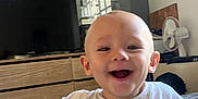 Camille a rejoint le concours — aidez-le/la à gagner de superbes lots ! baby, smiling, child, indoor, white_shirt, blanket, furniture, television, window, fan, wooden_drawer, happy, face, head, person, room, home, laughing, cute, toddler