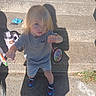 child, blonde_hair, concrete, steps, shadow, crafts, holding, outdoor, sunny, shoes, spider_man, casual_clothing, serious_expression, sidewalk, grass, toy, person, young_child, summer, playtime