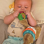 Ryder joined the competition — help win amazing prizes! baby, child, toy, plush, shirt, pants, shark_pattern, truck_pattern, bed, blanket, infant, cute, soft_toy, lying_down, indoors, playful, colorful, hands, face, focus