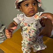 A'Layla is registered to the contest to win money with this photo: toddler, child, baby, hat, floral, overalls, table, hand, indoor, person, clothing, shoes, expression, face, skin, young, standing, support, furniture, curious