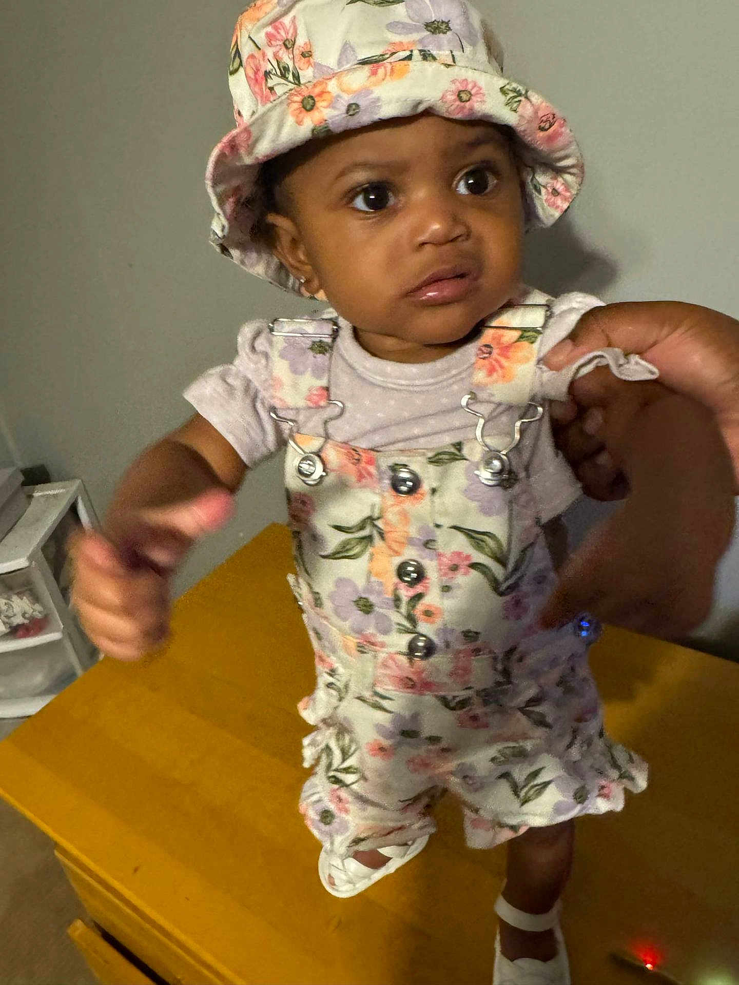 A'Layla is registered to the contest to win money with this photo: toddler, child, baby, hat, floral, overalls, table, hand, indoor, person, clothing, shoes, expression, face, skin, young, standing, support, furniture, curious