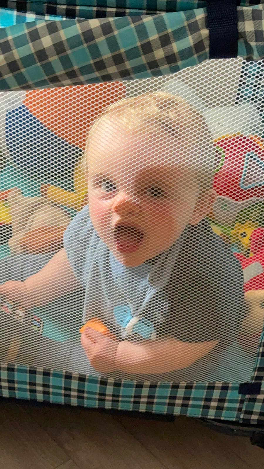 Tye is registered to the contest to win money with this photo: baby, child, playpen, mesh, toy, indoor, curious, expression, clothing, floor, checkered, pattern, colorful, soft, person, infant, cute, hand, face, mouth