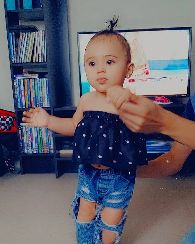 Riley joined the competition — help win amazing prizes! baby_toddler_clothing, bookcase, eye, finger, gesture, hair, happy, human_body, jean_short, joint, leg, neck, person, shelf, shorts, shoulder, skin, sleeve, standing, thigh