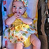 baby, infant, child, yellow_dress, bow, sunflower_pattern, smiling, cute, hands_clasped, baby_seat, colorful, happy, chubby_cheeks, portrait, indoors, soft_lighting, person, young_child, adorable, relaxed