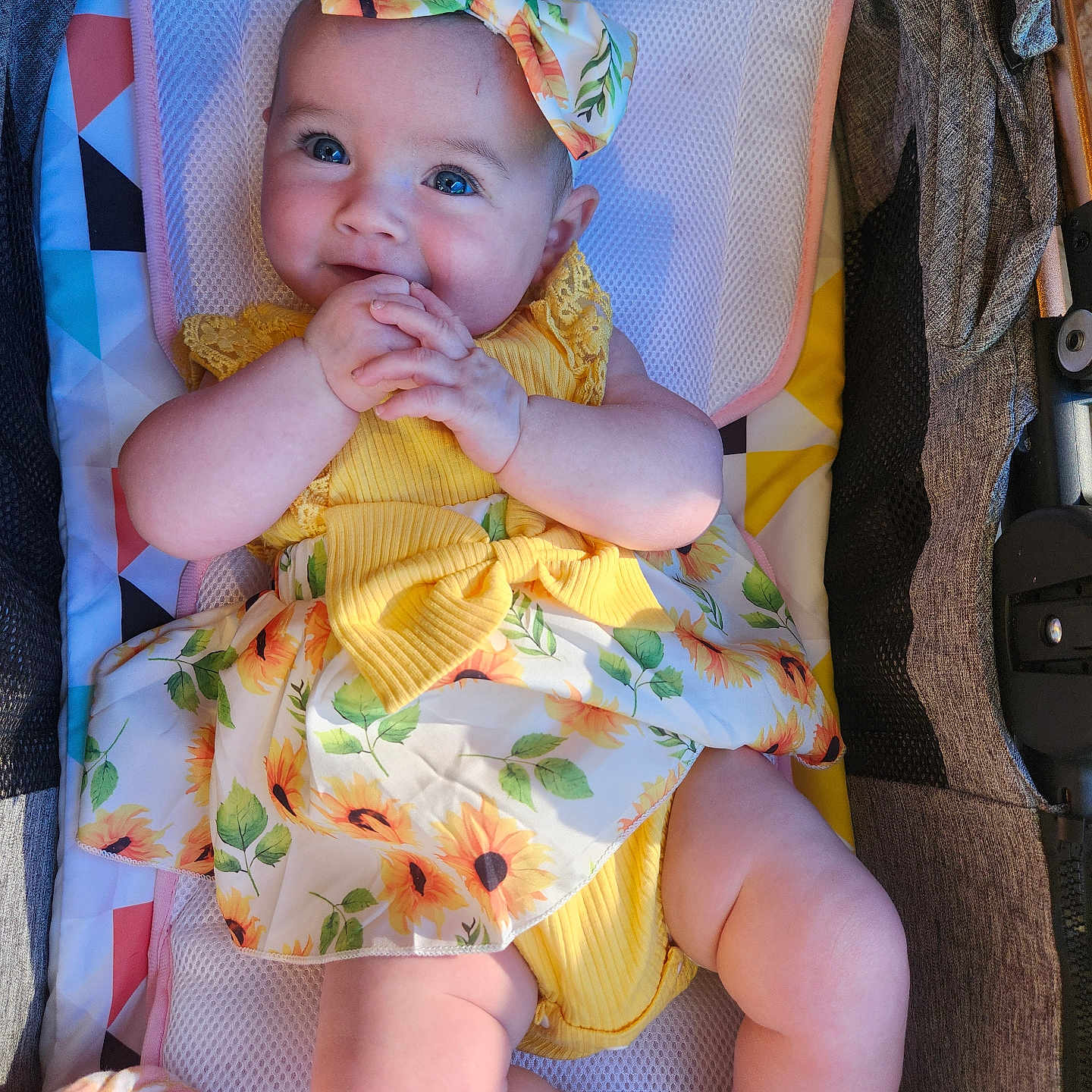 Jazmine joined the competition — help win amazing prizes! baby, infant, child, yellow_dress, bow, sunflower_pattern, smiling, cute, hands_clasped, baby_seat, colorful, happy, chubby_cheeks, portrait, indoors, soft_lighting, person, young_child, adorable, relaxed