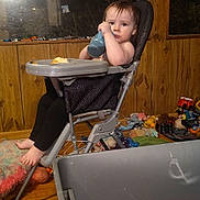 Lilith is registered to the contest to win money with this photo: toddler, high_chair, bottle, toy, indoor, child, face, wood_paneling, window, blanket, floor, plastic_bin, stuffed_toy, foot, legs, clothing, reflection, container, messy, home