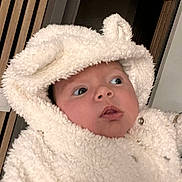 Emmy participe au concours pour gagner de l'argent avec cette photo : baby, infant, hood, fluffy, onesie, coat, eyes, surprised_expression, closeup, portrait, indoor, wooden_slats, doorway, warm, soft_texture, button, face, person, cheeks, cozy