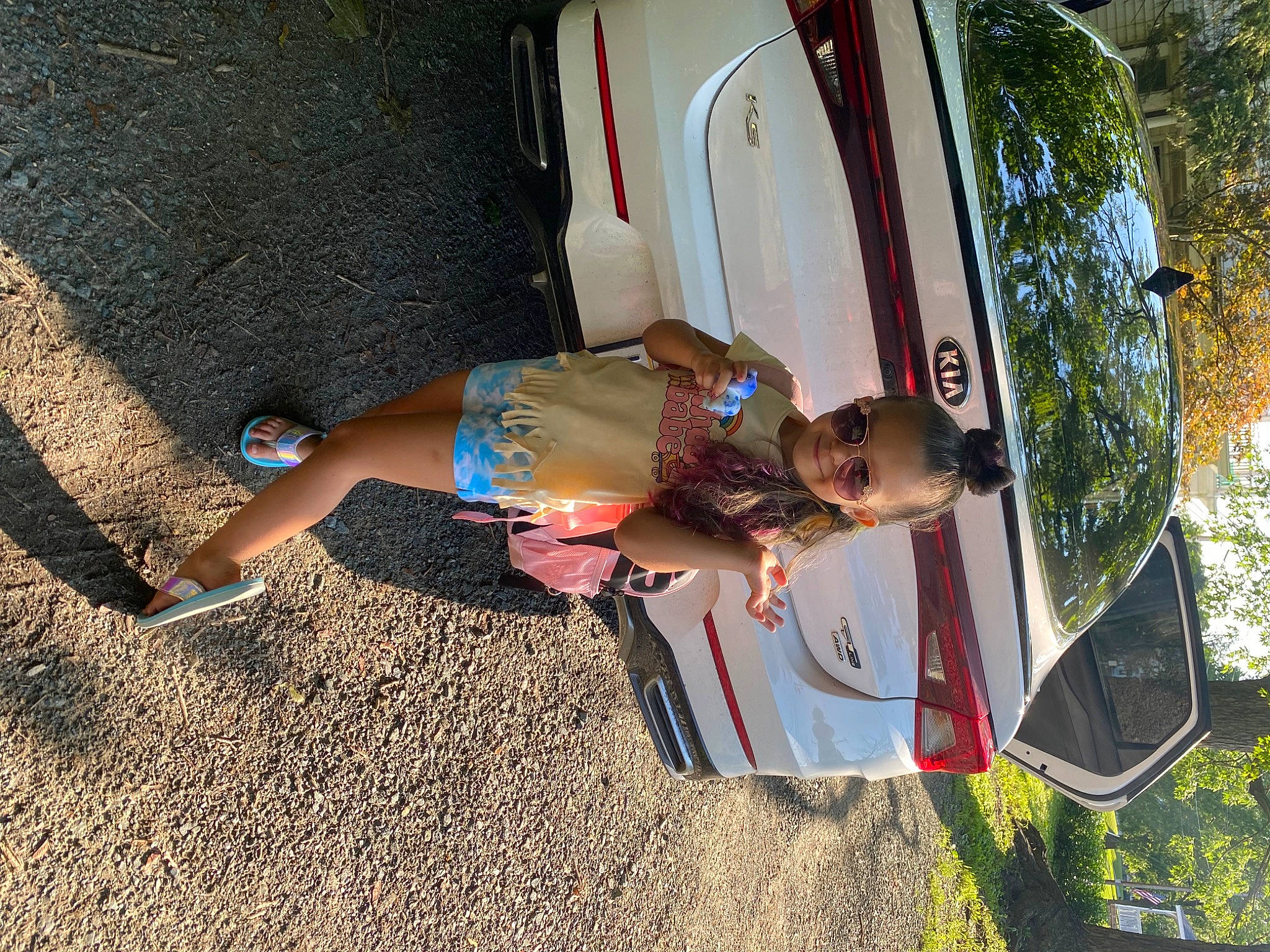 Khloe is registered to the contest to win money with this photo: automotive_exterior, automotive_lighting, automotive_tire, car, fun, grass, human_leg, joy, leisure, motor_vehicle, person, plant, recreation, shorts, thigh, tints_and_shades, tire, toddler, tree, vehicle