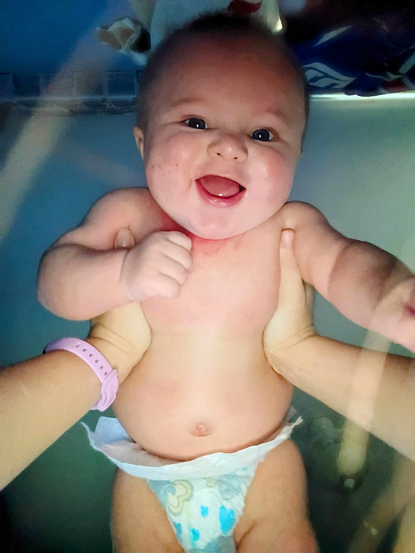 Elric is registered to the contest to win money with this photo: baby, smiling, diaper, water, hands, bath, infant, joyful, cute, skin, person, child, happy, face, expression, splash, holding, playful, blue_background, closeup