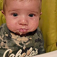 Logan joined the competition — help win amazing prizes! baby, child, messy, food, high_chair, face, clothing, camouflage, expression, indoor, portrait, young, infant, cute, eyes, mouth, seat, table, feeding, person
