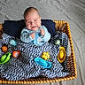 baby, basket, blanket, toy, toys, blue_clothing, smile, infant, happy, wicker, pattern, chevron, indoor, child, cute, playful, colorful, face, person, portrait