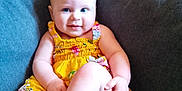 Iris is registered to the contest to win money with this photo: baby, child, infant, yellow_dress, couch, sofa, smile, legs, crossed_legs, indoor, home, cute, happy, person, face, blue_eyes, diaper, plush, seated, comfort