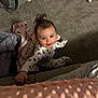 baby, infant, child, onesie, bow_pattern, smile, looking_up, hand_on_couch, blanket, floral_blanket, pink_blanket, carpet, backpack, baby_items, hair_tuft, candid, indoor, portrait, cozy, floor