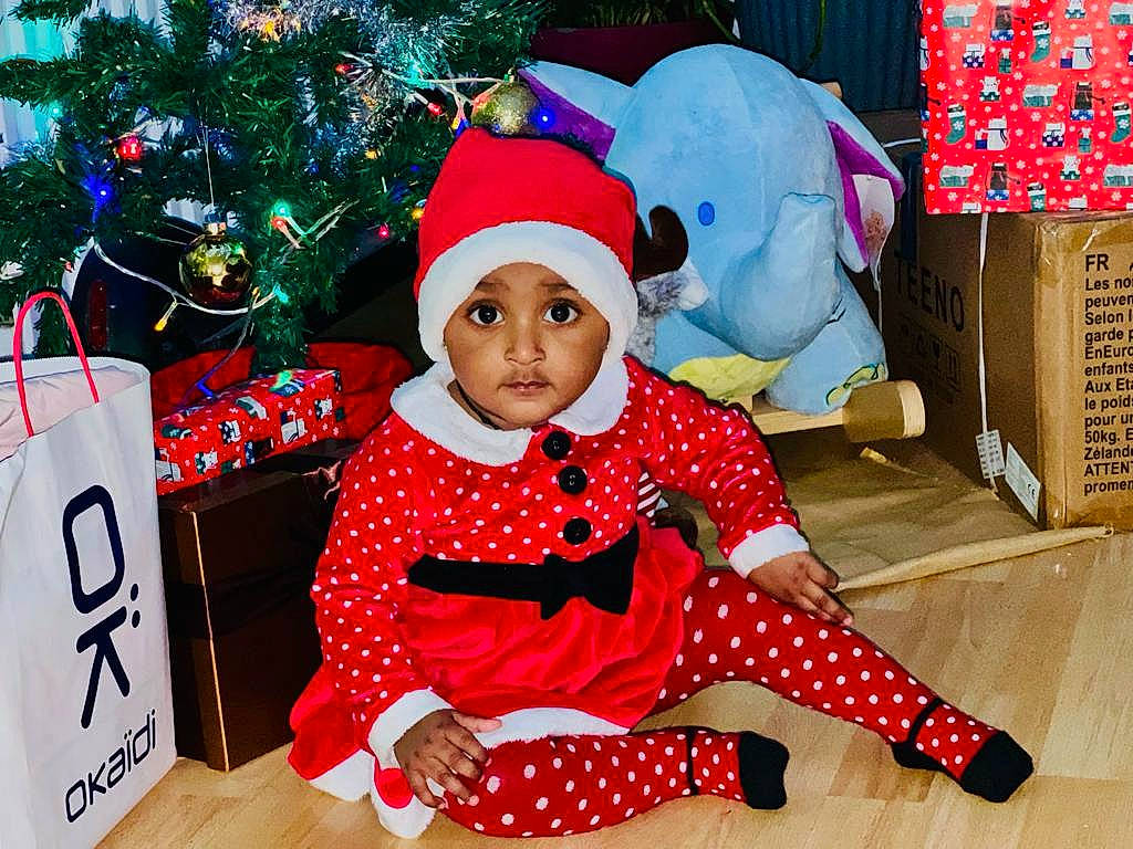 Sathursika participe au concours pour gagner de l'argent avec cette photo : baby, baby_toddler_clothing, carmine, child, christmas, christmas_decoration, christmas_eve, christmas_tree, costume_hat, event, fictional_character, fun, happy, headwear, holiday, lap, pattern, person, red, sleeve