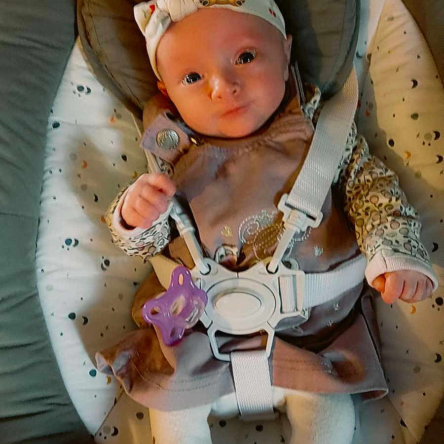 Hanaya participe au concours pour gagner de l'argent avec cette photo : adorable, baby, baby_seat, boots, child, clothing, cozy, cute, face, headband, indoor, infant, pacifier, person, plush, smiling, soft_lighting, straps, toddler, warm_colors