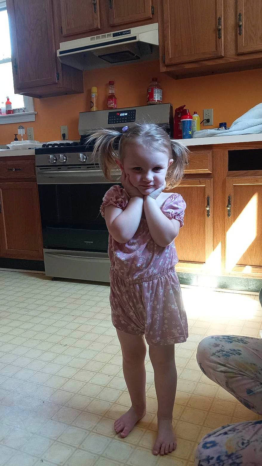 Nikki is registered to the contest to win money with this photo: cabinetry, child, cooktop, countertop, dress, floor, flooring, gas_stove, happy, hardwood, home_appliance, kitchen, kitchen_appliance, kitchen_stove, leg, one_piece_garment, person, shoulder, stove, toddler