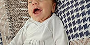 Léandro participe au concours pour gagner de l'argent avec cette photo : baby, infant, smiling, clothing, white_shirt, gray_pants, lying_down, patterned_quilt, happy, face, hand, soft_texture, cute, newborn, young_child, indoors, cozy, expression, person, child