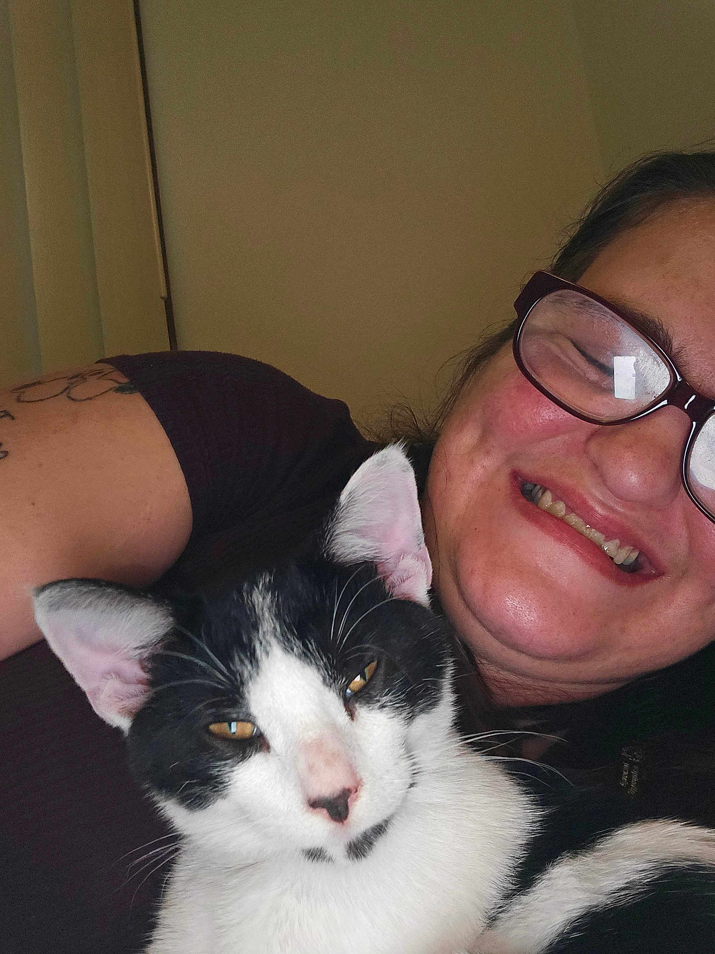 Angel Joy is registered to the contest to win money with this photo: animal, black_and_white_cat, cat, closeup, comfortable, content, cozy, eyewear, facial_expression, glasses, happy, human, indoor, person, pet, portrait, relaxed, smile, snuggle, tattoo