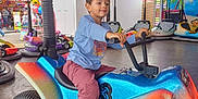 Naëlyo a rejoint le concours — aidez-le/la à gagner de superbes lots ! child, amusement_park, bumper_car, ride, colorful, lights, fun, playful, casual_clothing, sneakers, indoor, entertainment, young_boy, vehicle, toy, smile, activity, leisure, happy, person