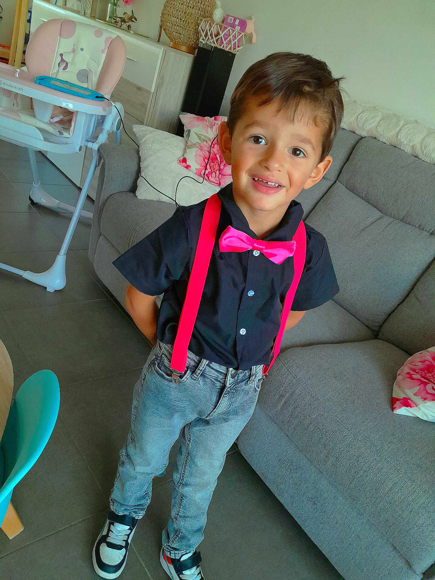 Naëlyo a rejoint le concours — aidez-le/la à gagner de superbes lots ! child, boy, smiling, indoor, standing, black_shirt, pink_suspender, bow_tie, jeans, sneakers, couch, pillow, high_chair, floor_tile, home, furniture, happy, casual, portrait, fashion