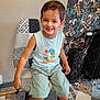 child, boy, smile, sitting, chair, patchwork, indoor, floor, patterned_floor, wallpaper, floral_wallpaper, shorts, sandals, clothing, happy, portrait, person, casual, home, furniture