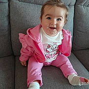 Soëlya a rejoint le concours — aidez-le/la à gagner de superbes lots ! baby, child, smiling, pink_clothing, socks, ponytail, couch, indoor, happy, cute, face, person, seated, casual, young, infant, toddler, apparel, portrait, home
