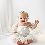 Anastasia is registered to the contest to win money with this photo: baby, child, infant, white_dress, lace, headband, blue_eyes, smiling, sitting, cute, soft_lighting, studio, portrait, barefoot, innocent, curious, tulle_skirt, bright_background, bokeh, happy