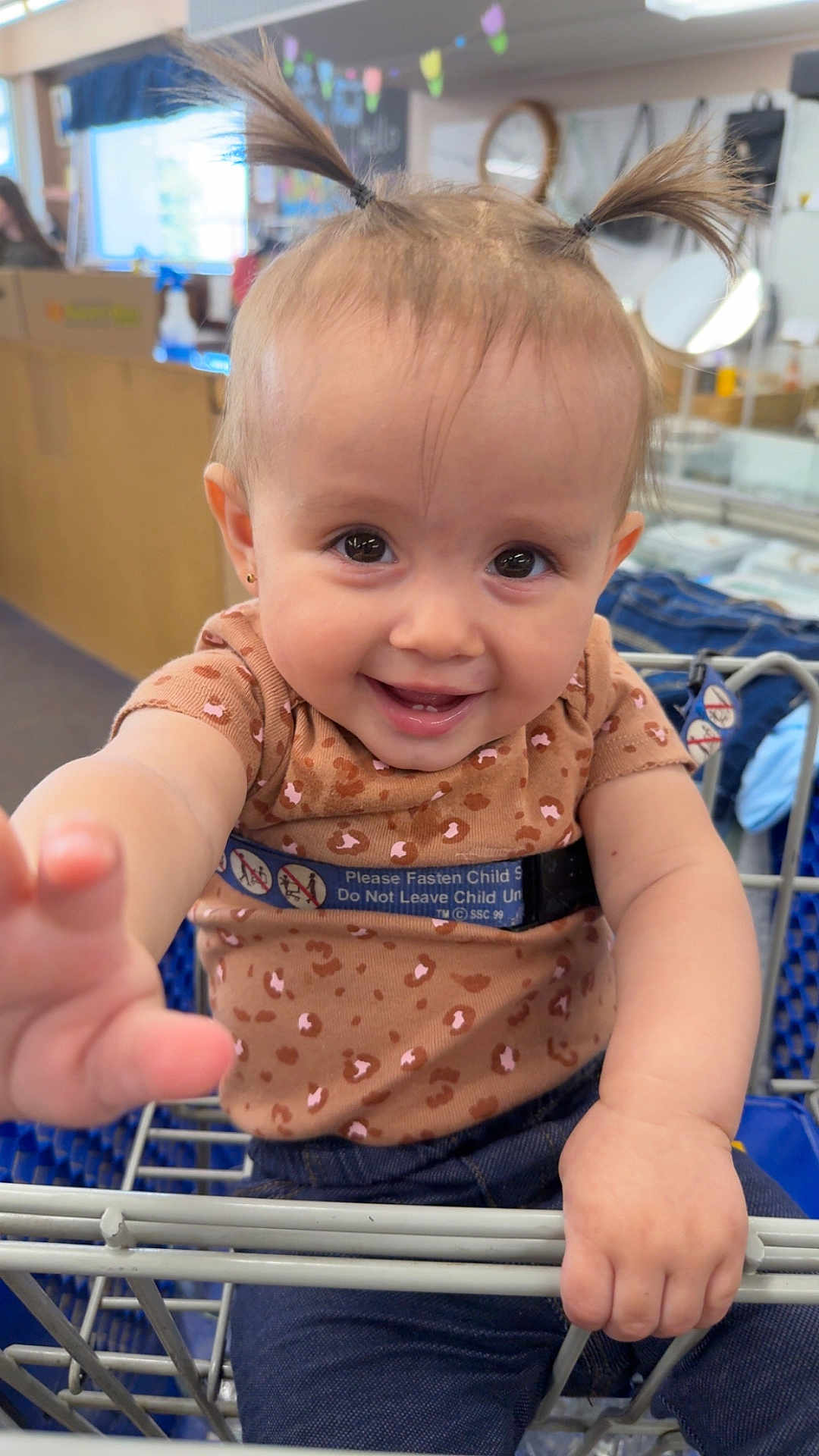 Allyanna joined the competition — help win amazing prizes! baby, child, shopping_cart, pigtails, smiling, cute, indoor, clothing, jeans, leopard_print, person, hand, face, happy, retail, store, seatbelt, metal, holding, portrait