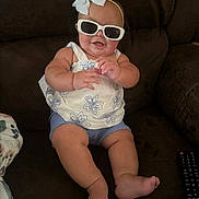 Mollie joined the competition — help win amazing prizes! baby, blue_shorts, bow, child, clothing, couch, cute, face, foot, hand, happy, headband, indoor, person, remote_control, sitting, skin, smiling, sunglasses, white_top