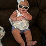 baby, blue_shorts, bow, child, clothing, couch, cute, face, foot, hand, happy, headband, indoor, person, remote_control, sitting, skin, smiling, sunglasses, white_top