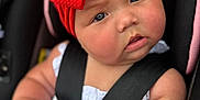 Mollie is registered to the contest to win money with this photo: baby, infant, red_bow, headband, car_seat, white_clothing, blanket, curious_expression, child, seatbelt, closeup, face, skin, arm, hand, indoor, portrait, cute, chubby_cheeks, young