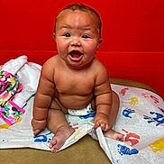 Mollie joined the competition — help win amazing prizes! baby, child, diaper, sitting, happy, smiling, handprint, colorful, red_wall, skin, cute, infant, playful, indoors, expression, face, person, bare_chest, toddler, blanket