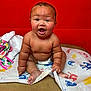 baby, child, diaper, sitting, happy, smiling, handprint, colorful, red_wall, skin, cute, infant, playful, indoors, expression, face, person, bare_chest, toddler, blanket