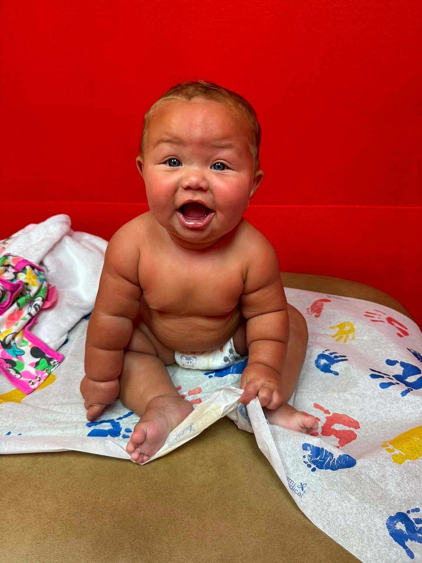 Mollie joined the competition — help win amazing prizes! baby, child, diaper, sitting, happy, smiling, handprint, colorful, red_wall, skin, cute, infant, playful, indoors, expression, face, person, bare_chest, toddler, blanket