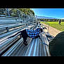 Akanahe is registered to the contest to win money with this photo: animal, bleachers, blue_sky, casual, daytime, dog, fence, grass, jacket, leash, metal, mountains, outdoor, park, person, pet, side_view, sports_field, sunny, walking