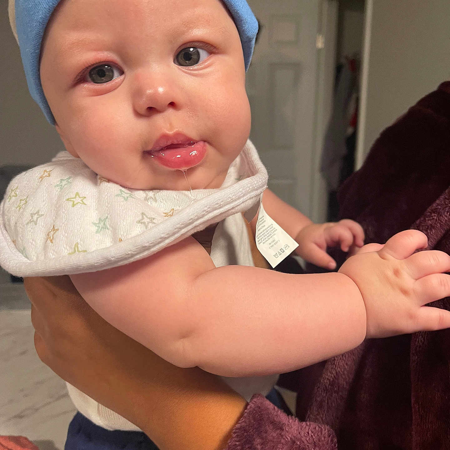 Demilo Johnson is registered to the contest to win money with this photo: adult_hand, baby, bib, blue_beanie, chubby_cheeks, closeup, clothing, curious, door, drool, expression, fabric, face, hand, holding, indoor, infant, person, skin, soft_lighting