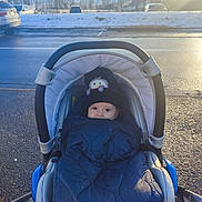 Iyed a rejoint le concours — aidez-le/la à gagner de superbes lots ! baby, stroller, blanket, hat, winter, snow, outdoor, child, cold, bundle, parking_lot, car, sunlight, clothing, face, person, daytime, road, warm, cute
