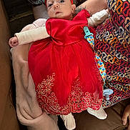 Scarlet joined the competition — help win amazing prizes! baby, red_dress, headband, blanket, person, patterned_clothing, couch, indoor, infant, soft_texture, comfort, seated, cute, child, holding, footwear, pacifier_clip, colorful, fabric, young_child