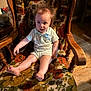 baby, child, chair, wooden_chair, floral_pattern, vintage, indoors, curious, expression, hair, wild_hair, sitting, foot, armrest, wood_floor, lighting, portrait, person, clothing, cute