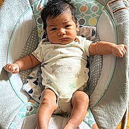 Ethan is registered to the contest to win money with this photo: baby, infant, face, arms, legs, foot, baby_seat, clothing, onesie, pattern, wood_floor, indoor, person, newborn, cute, expression, hair, skin, comfort, child