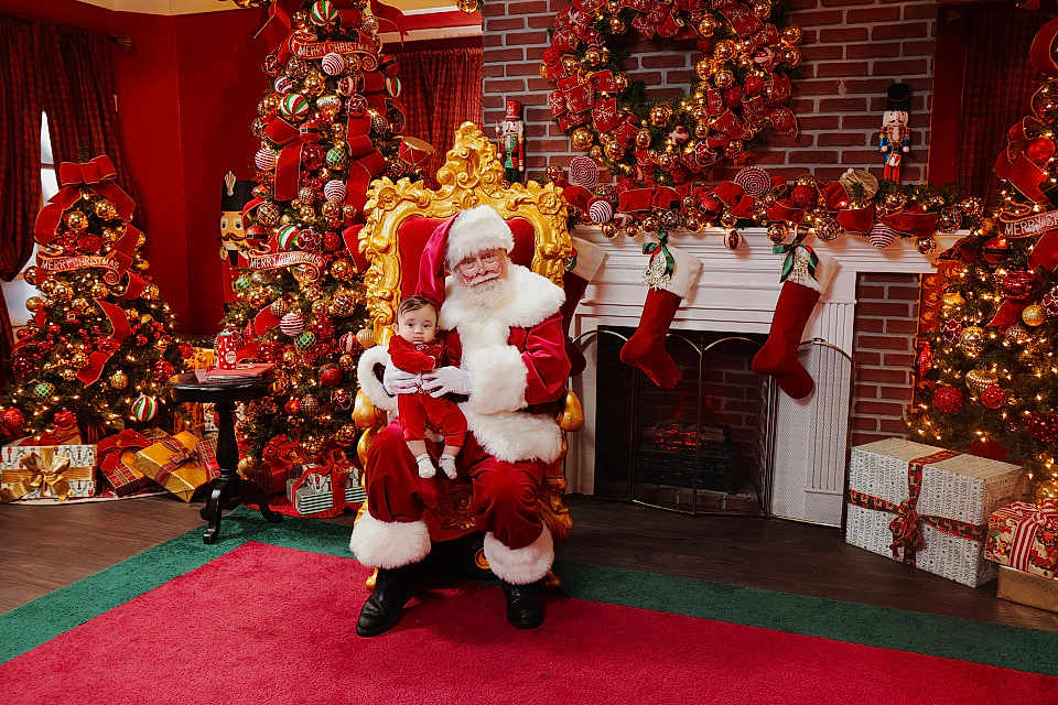 David is registered to the contest to win money with this photo: santa_claus, baby, christmas_tree, christmas_decorations, wreath, stockings, gifts, holiday, festive, red_carpet, golden_chair, fireplace, brick_wall, indoor, celebration, person, child, smiling, holiday_spirit, winter