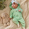 baby, infant, hoodie, headband, white_bow, plush_toy, bunny, blanket, soft_texture, greenery, cute, child, laying_down, cozy, comfortable, indoor, portrait, clothing, socks, adorable