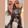 Sugar is registered to the contest to win money with this photo: person, cat, kitten, tortoiseshell_cat, pet, indoor, smiling, holding, tattoo, collar, animal, cute, face, fur, closeup, portrait, young_adult, warm_lighting, casual_clothing, home