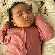 Adanna is registered to the contest to win money with this photo: baby, sleeping, pink_clothing, curly_hair, infant, cozy, cushion, baby_lounger, pattern, tree_design, soft_texture, peaceful, newborn, child, portrait, indoors, cute, resting, toddler, comfort